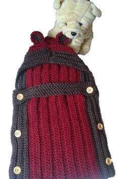 a teddy bear sitting on top of a red and black knitted bag with buttons