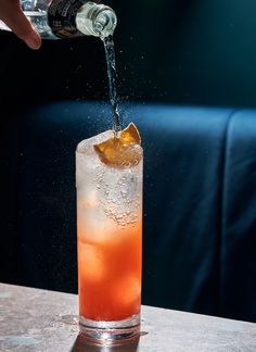 a person pouring water into a glass filled with ice and orange juice on top of a table