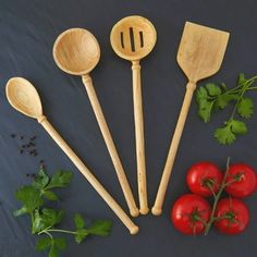 four wooden spoons and three tomatoes on a black surface with parsley, pepper, cherry tomatoes and green leaves