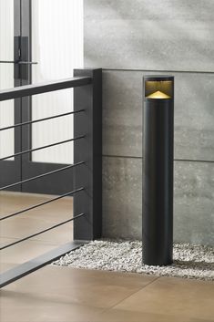 a black post with a light on it next to a wall and stairs in front of a building