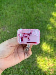 a hand holding a small pink case with scissors on it