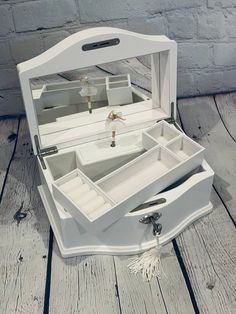 an open white jewelry box sitting on top of a wooden floor next to a brick wall