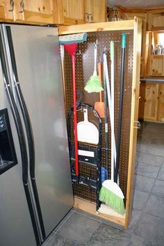 a refrigerator with brooms, mop and cleaning supplies in it next to cabinets