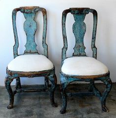 two old chairs with white cushions are sitting side by side in front of a wall