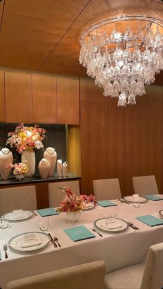 a dining room table is set with place settings and flowers in vases on the wall