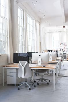 an office with multiple desks and chairs in front of two large windowed windows