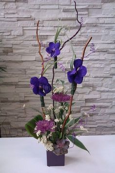 a vase with purple flowers and greenery on a table