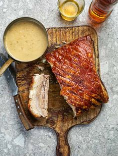 a wooden cutting board topped with meat next to two glasses of beer and a knife