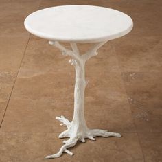 a small white table sitting on top of a wooden floor next to a planter