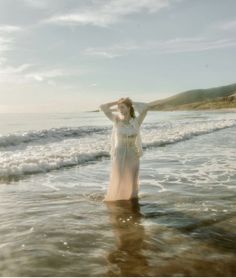 a woman is standing in the water at the beach with her hands on her head