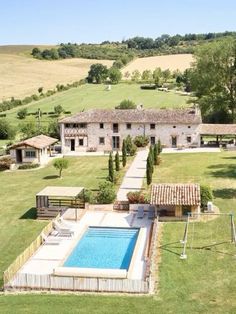 an aerial view of a house with a swimming pool in the foreground and surrounding fields