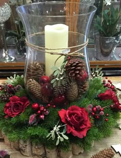 a glass vase filled with pine cones and red flowers sitting on top of a table