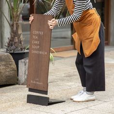 a woman leaning on a sign that says coffee cake soup sandwich