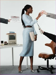 a woman standing in front of a desk with a computer and other people around her