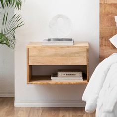 a bed with a white comforter next to a wooden night stand on top of a hard wood floor