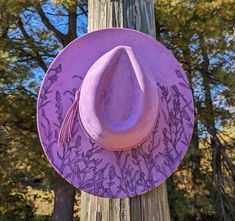 This truly one-of-a-kind hand burnt fedora is perfect to add a stylish flare to your outfit or hang as a unique floral wall decoration. The hat is a stunning shade of lilac that's sure to make any outfit stand out. It's burned entirely by hand using a pyrography tool with an original and entirely freehanded design (never using a stencil or laser machine.) The pastel purple faux suede material burns a gorgeous deep shade of purple. This design features lavender flowers growing up from the bottom of the brim with the look of a gentle gust of wind blowing through them. I adjusted the woodburner to different temperatures to achieve realistic shading and depth upon the petals and leaves of the flowers. Lastly, this hat is adorned with a purple faux leather braided hat band.  Hat has a crown siz Adjustable Lavender Hat With Curved Brim, Purple Wide Brim Festival Hat, Purple Handmade Hat With Short Brim, Adjustable Flat Brim Purple Felt Hat, Adjustable Lavender Brimmed Hat, Purple Bohemian Brimmed Hat, Cottagecore Gifts, Wide Brim Fedora, Cowgirl Hats