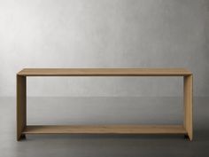 an empty wooden table on a gray floor with concrete walls in the background and light colored wood furniture