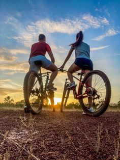 two people riding bikes in the middle of a field at sunset or sunrise with sun setting behind them