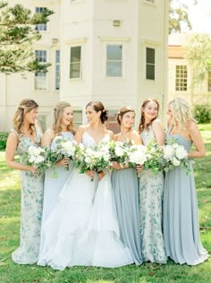 a group of women standing next to each other in front of a white house holding bouquets