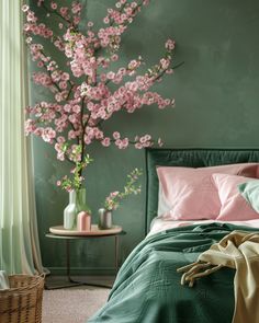 a bedroom with green walls and pink flowers in vases on the side table next to the bed