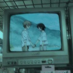 two people standing in front of an old tv with the screen showing anime on it