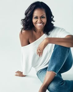 a woman in white shirt and jeans sitting on the ground with her legs spread out