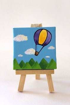 an easel with a painting on it and a hot air balloon in the sky