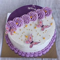 a white cake with purple icing and butterflies on it, sitting on a table