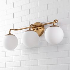 three white balls are hanging from a brass finish light fixture on a brick wall in an empty room