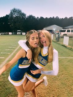 two cheerleaders posing for a photo on the field with their arms around each other