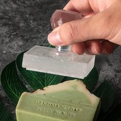 a hand holding a soap bar over a leafy green object with the word, handmade soap on it