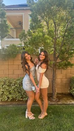 two beautiful young women standing next to each other in front of a tree and building