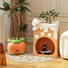 the cat house is next to two potted plants and an orange plant in it