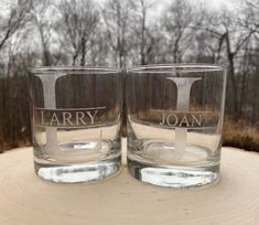 two glasses sitting on top of a wooden table next to each other in front of trees