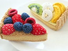 two crocheted slices of pie on a plate with strawberries and blueberries