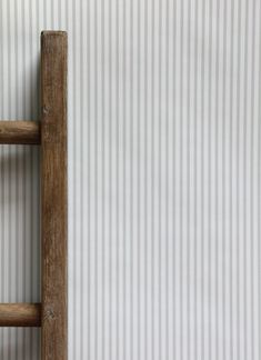 an old wooden ladder leaning against a wall with vertical stripes on the wall behind it