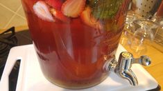 a pitcher filled with liquid and strawberries on top of a white tray next to a stove