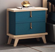 a night stand with two drawers and a gold object on top, next to a bed