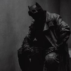 black and white photograph of a man in a batman costume sitting on a toilet seat