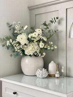 a white vase filled with flowers sitting on top of a dresser