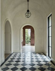 an empty hallway with black and white checkered flooring, arched doorways and windows