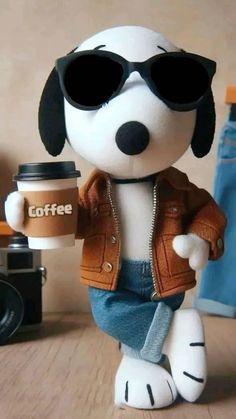 a stuffed dog holding a coffee cup and wearing sunglasses on top of a wooden table