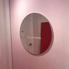 a round mirror mounted to the side of a pink wall next to a white door