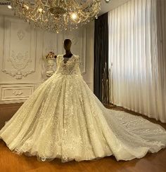 a white wedding dress on display in a room with chandelier and curtained windows