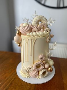 there is a white cake with pink and gold decorations on the top, sitting on a wooden table