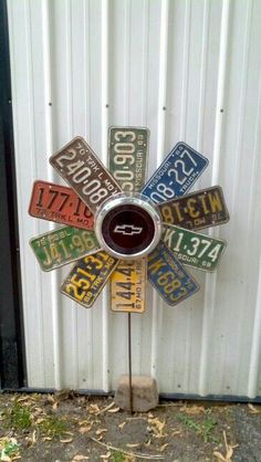 a metal flower with multiple license plates attached to it's center piece, in front of a white wall