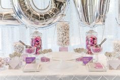 a table topped with lots of candy and confetti next to giant silver balloons