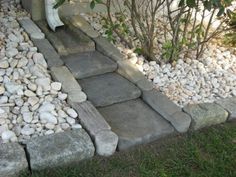 a stone walkway made out of rocks and stones in front of a house with shrubbery