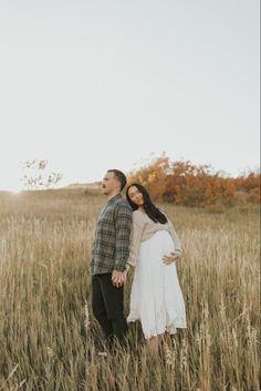 a pregnant couple standing in the middle of a field with their arms around each other