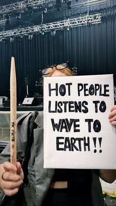 a woman holding up a sign that says hot people listen to wave to earth